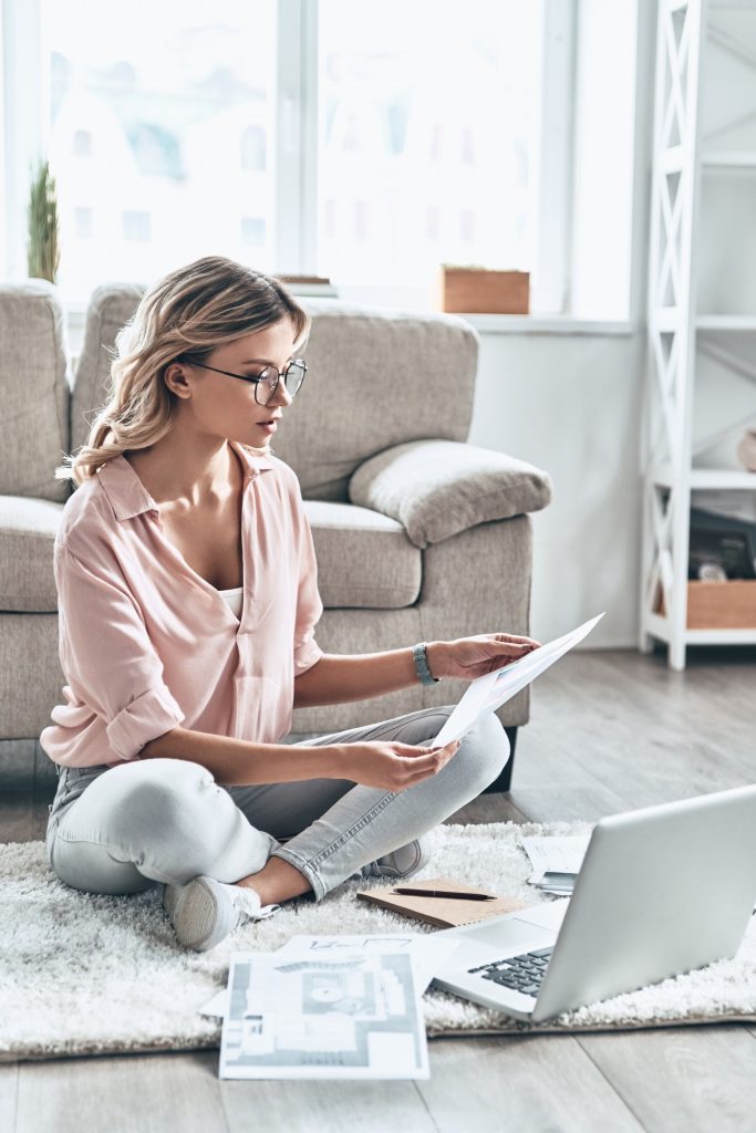 Another working day. Thoughtful young woman in eyewear working with documents while flooring at home